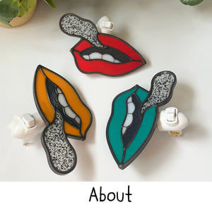 An image of three nightlights depicting mouths with red, pumpkin, or teal color lips, each with a black and white speckle glass coming out of them in the shape of a speech bubble. The word "About" is at the bottom of the image